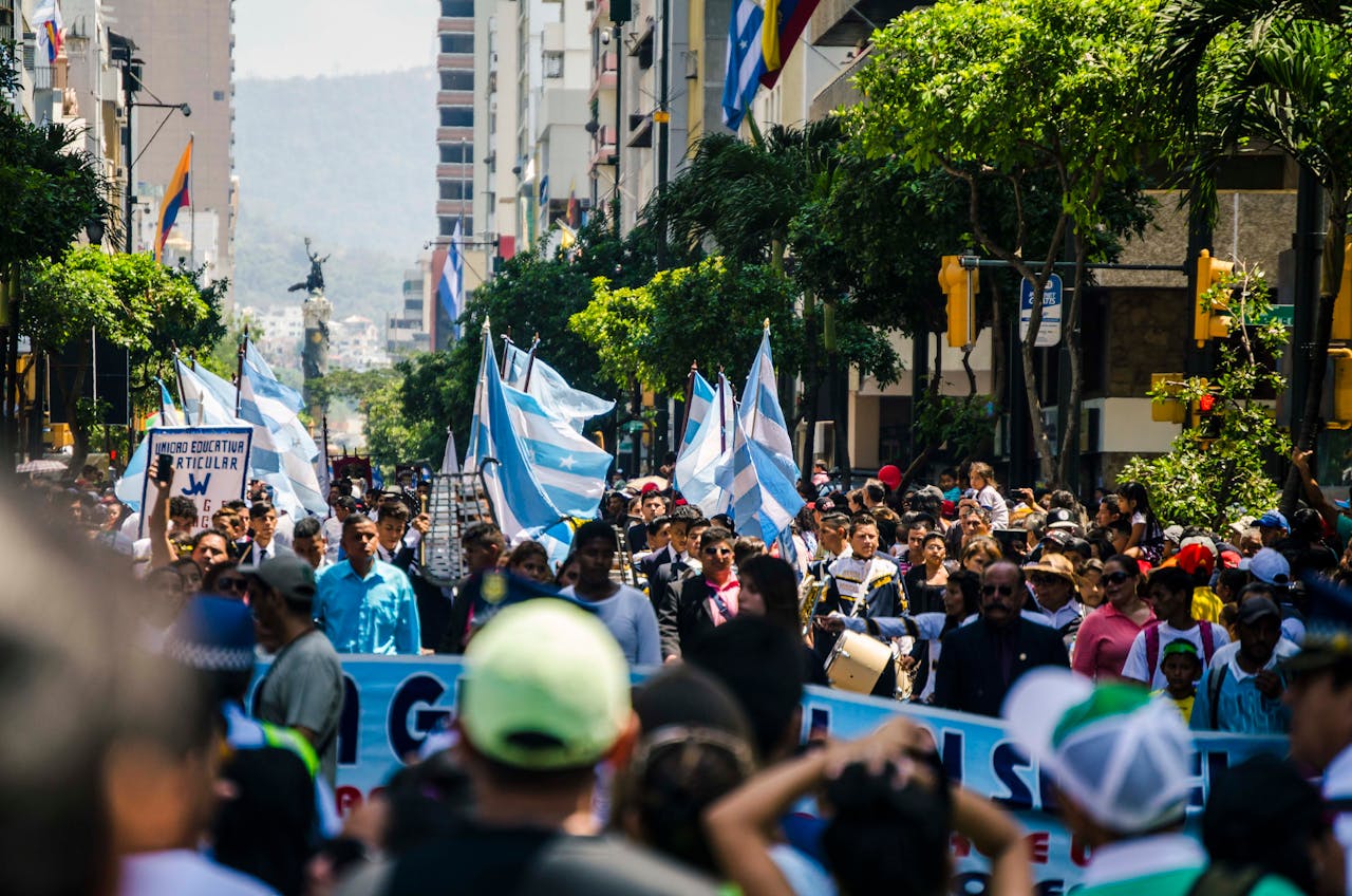 A lively urban protest with people holding flags and signs on a sunny day.