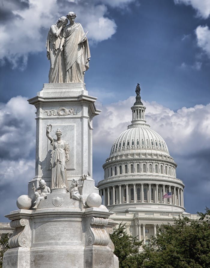 US Capitol building with Peace Monument statue under dramatic clouds.